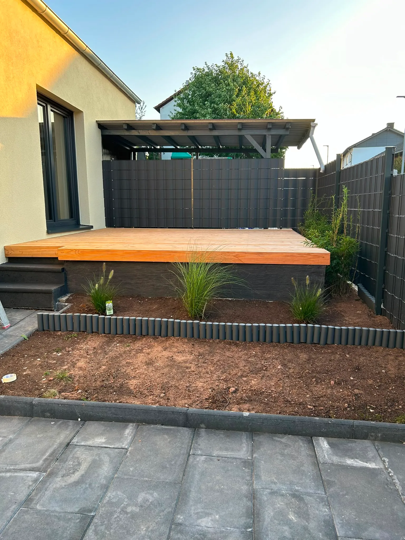 Holzterrasse mit anthrazitfarbenem Sichtschutz und neu angelegtem Beet.